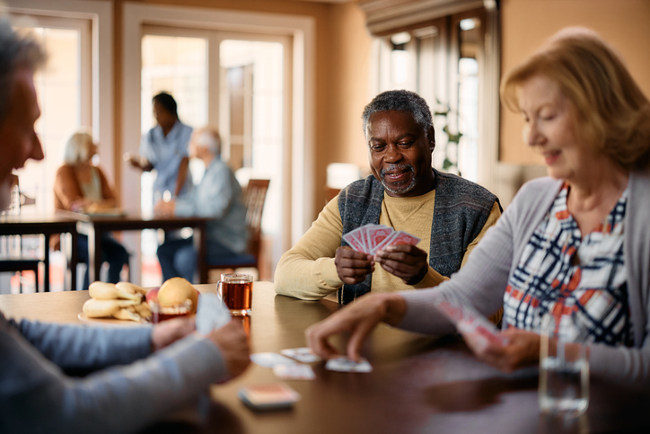 A group of senior adults engaged in a card game at a table, with snacks and drinks in front of them.